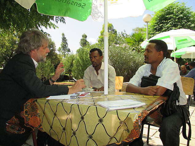 Three men sitting at a table under an umbrella.