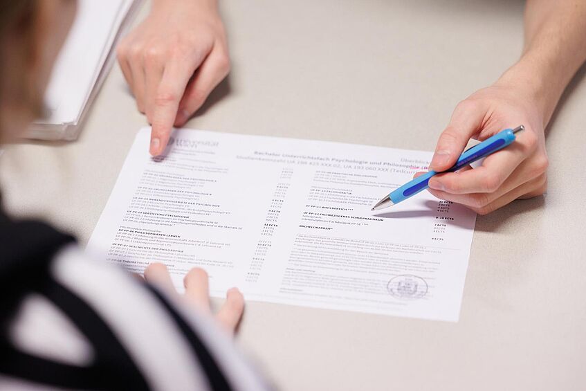 Nahansicht eines SSC-Mitarbeiters, der mit Stift und Finger Informationen auf einem Zettel zeigt